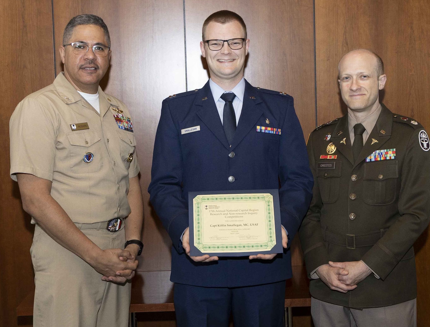 U.S. Navy Capt. Juan Rosario (left), Chief of Staff at Walter Reed National Military Medical Center, and U.S. Army Lt. Col. Michael Orestes (right), Director for Education, Training and Research at Walter Reed, recognize U.S. Air Force (Dr.) Capt. Kiffin Smallegan, of the Department of Pediatrics, for earning first place in the Department of Research Programs' annual poster competition in the evidence-based practice category. The annual competition highlights research conducted by Walter Reed's staff, interns, residents and fellows.
