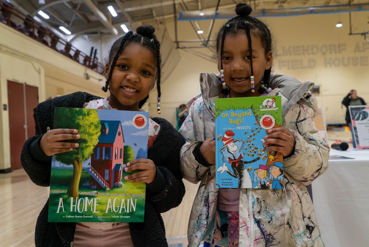 Two young girls hold out books in front of them.