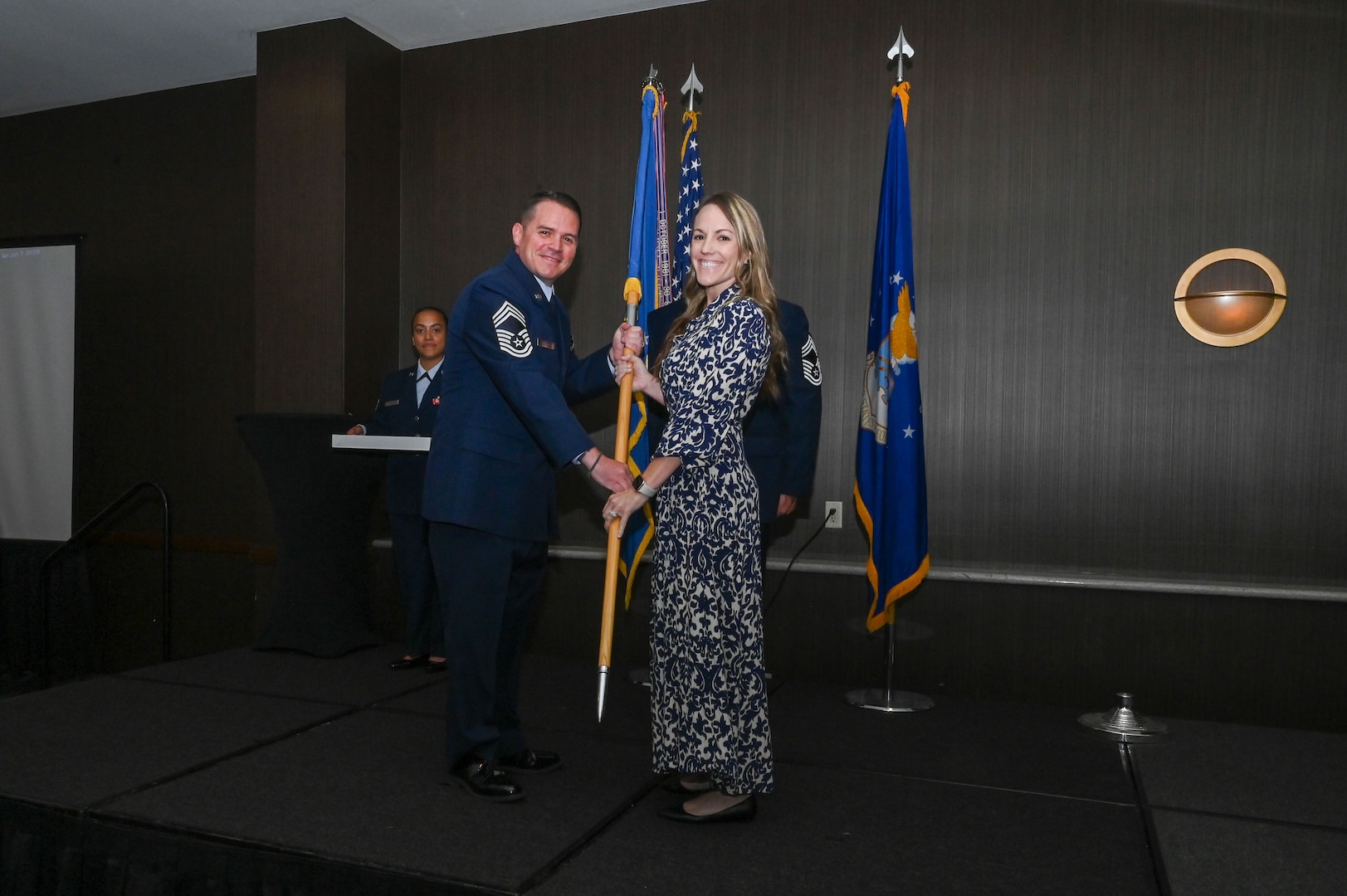 Chief Master Sgt. Kurtis Albright, 433rd Aircraft Maintenance Squadron senior leader, hands the 433rd Airlift Wing guidon to Morgan Harrison, Alpha Media director of sales, during the 433rd AW 2025 Honorary Commanders’ Induction Ceremony in San Antonio, June 7, 2025.