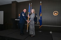 Chief Master Sgt. Kurtis Albright, 433rd Aircraft Maintenance Squadron senior leader, hands the 433rd Airlift Wing guidon to Morgan Harrison, Alpha Media director of sales, during the 433rd AW 2025 Honorary Commanders’ Induction Ceremony in San Antonio, June 7, 2025.