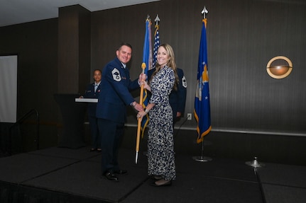 Chief Master Sgt. Kurtis Albright, 433rd Aircraft Maintenance Squadron senior leader, hands the 433rd Airlift Wing guidon to Morgan Harrison, Alpha Media director of sales, during the 433rd AW 2025 Honorary Commanders’ Induction Ceremony in San Antonio, June 7, 2025.