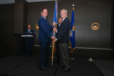 Maj. Alexander Williams, 433rd Contingency Response Flight commander, hands the 433rd Airlift Wing guidon to Duane Paulson, San Antonio independent consultant, during the 433rd AW 2025 Honorary Commanders’ Induction Ceremony in San Antonio, June 7, 2025.