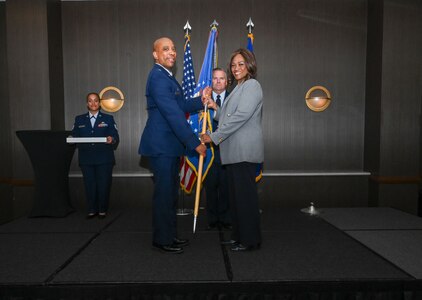 Lt. Col. Jason Cockrell, 68th Airlift Squadron commander, hands the 433rd Airlift Wing guidon to Vanessa J-Douglas, Masters Leadership Program San Antonio board of directors, during the 433rd AW 2025 Honorary Commanders’ Induction Ceremony in San Antonio, June 7, 2025.