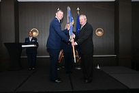 Maj. Aleksander Layne, 433rd Logistics Readiness Squadron commander, hands the 433rd Airlift Wing guidon to Jay Gilmore, SWBC Mortgage Company senior loan officer, during the 433rd AW 2025 Honorary Commanders’ Induction Ceremony in San Antonio, June 7, 2025.