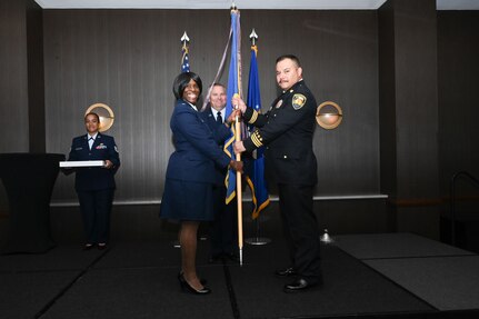 Lt. Col. Teanglia Moore, 26th Aerial Port Squadron commander, hands the 433rd Airlift Wing guidon to Rudy Khalaf, Bexar County division chief of fire protection, during the 433rd AW 2025 Honorary Commanders’ Induction Ceremony in San Antonio, June 7, 2025.