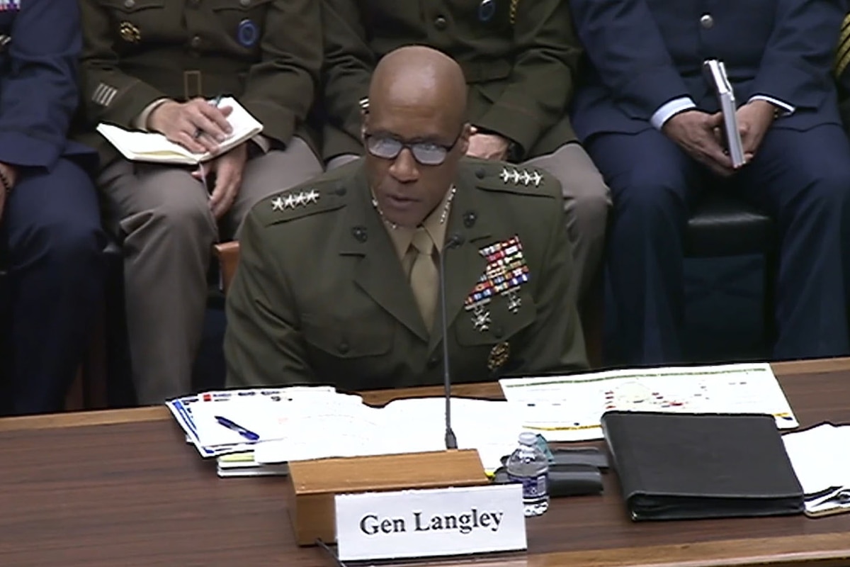 A man wearing a military uniform sits at a desk and speaks into a microphone.