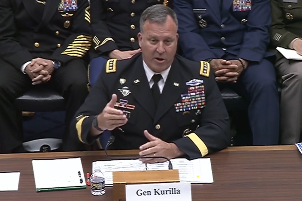 A man wearing a military uniform sits at a desk and speaks into a microphone.