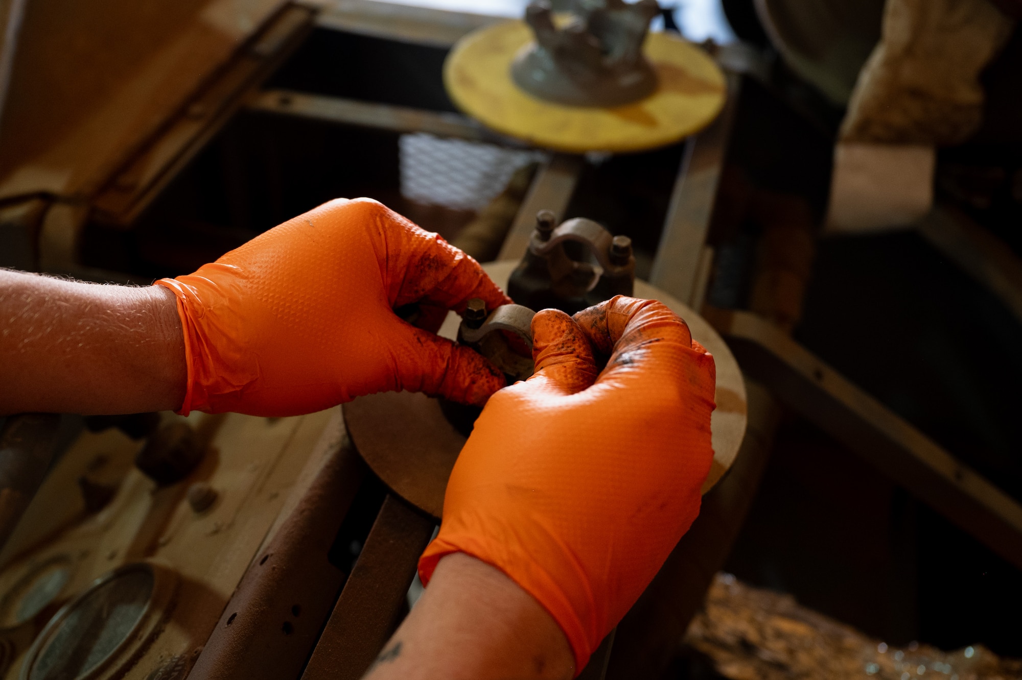 Airman wearing orange gloves removes a bolt from a brake disc