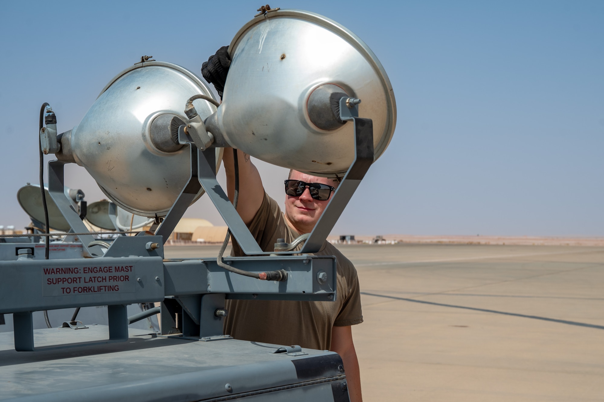 Airman adjusts a bulb on a flood light on a flightline
