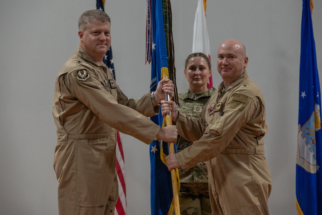 U.S. Air Force Brig. Gen. Richard Dickens, right, 379th Air Expeditionary Wing outgoing commander, passes the 379th AEW guidon to Maj. Gen. David Shoemaker, 9th Air Force (Air Forces Central) deputy commander, during the 379th AEW Change of Command Ceremony within the U.S. Central Command area of responsibility, June 9, 2025. The 379th AEW provides support to more than 5,400 Air Force, joint and coalition force partners. (U.S. Air Force photo by Staff Sgt. Sean Moriarty)