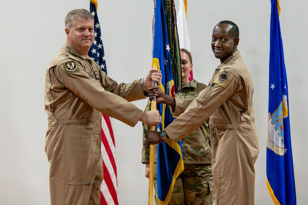 U.S. Air Force Brig. Gen. Travis Edwards, right, 379th Air Expeditionary Wing incoming commander, receives the 379th AEW guidon from Maj. Gen. David Shoemaker, 9th Air Force (Air Forces Central) deputy commander, during the 379th AEW Change of Command Ceremony within the U.S. Central Command area of responsibility, June 9, 2025. The 379th AEW provides support to more than 5,400 Air Force, joint and coalition force partners. (U.S. Air Force photo by Staff Sgt. Sean Moriarty)