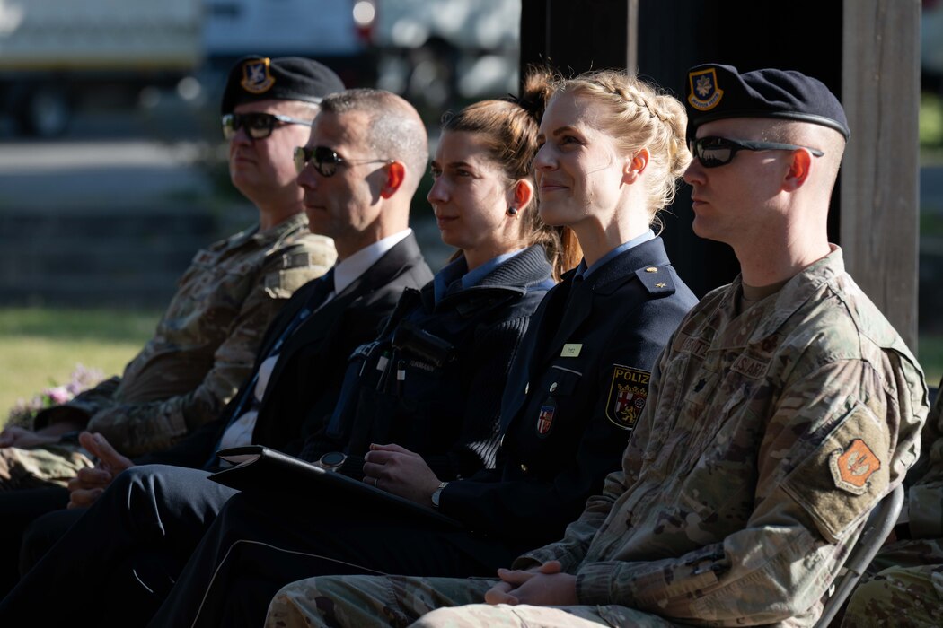 A group of Airmen and police officers listen to a speech being delivered at an outdoor ceremony.