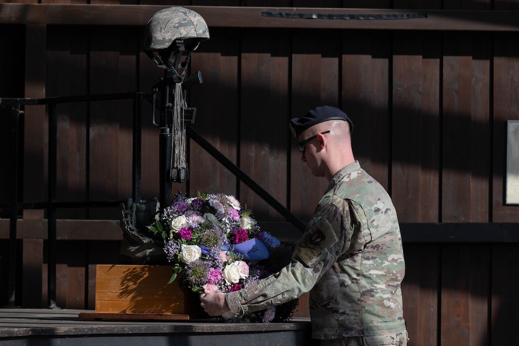 An Airman lays a flower wreath at the foot of a battle cross.