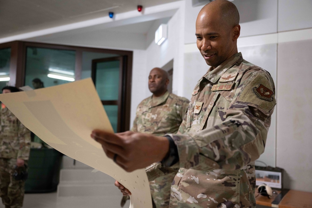 An Airman look at a paper target with bullet holes in it.
