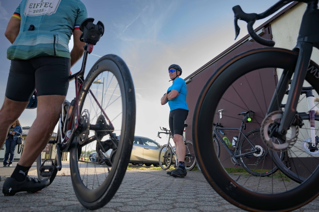 A cyclist stands between two bicycles and discusses the plans for the bike ride with other riders.