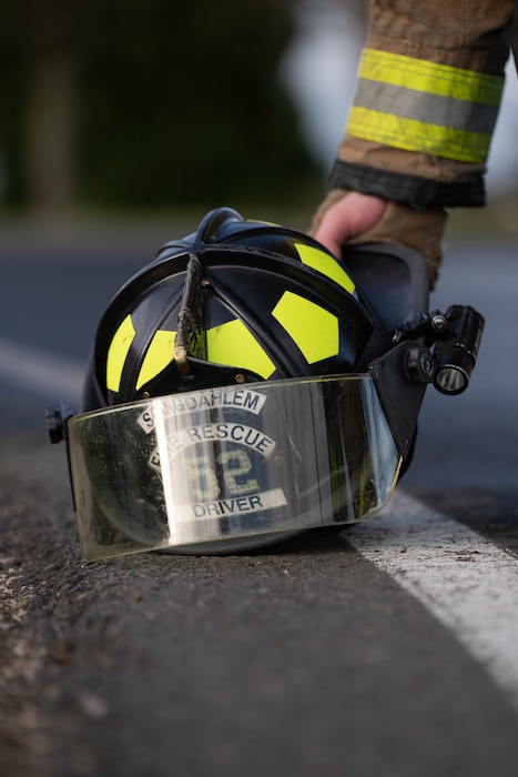 A firefighter picks up his helmet from the pavement.