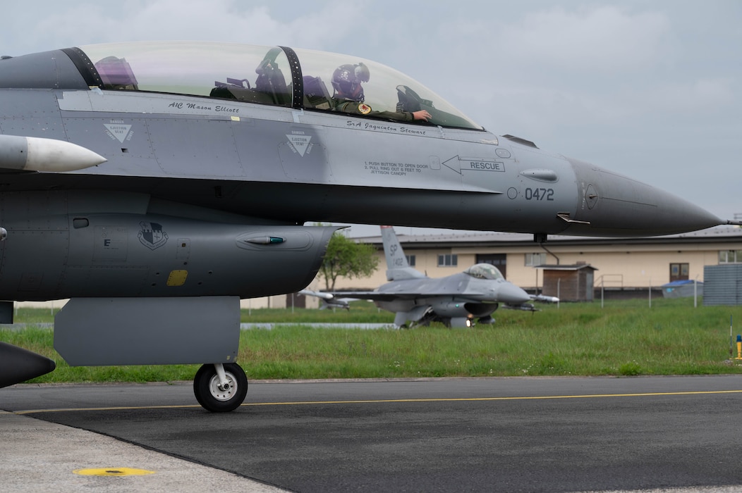 Two fighter aircraft parked adjacent to one another prepare to taxi towards the runway for flight.