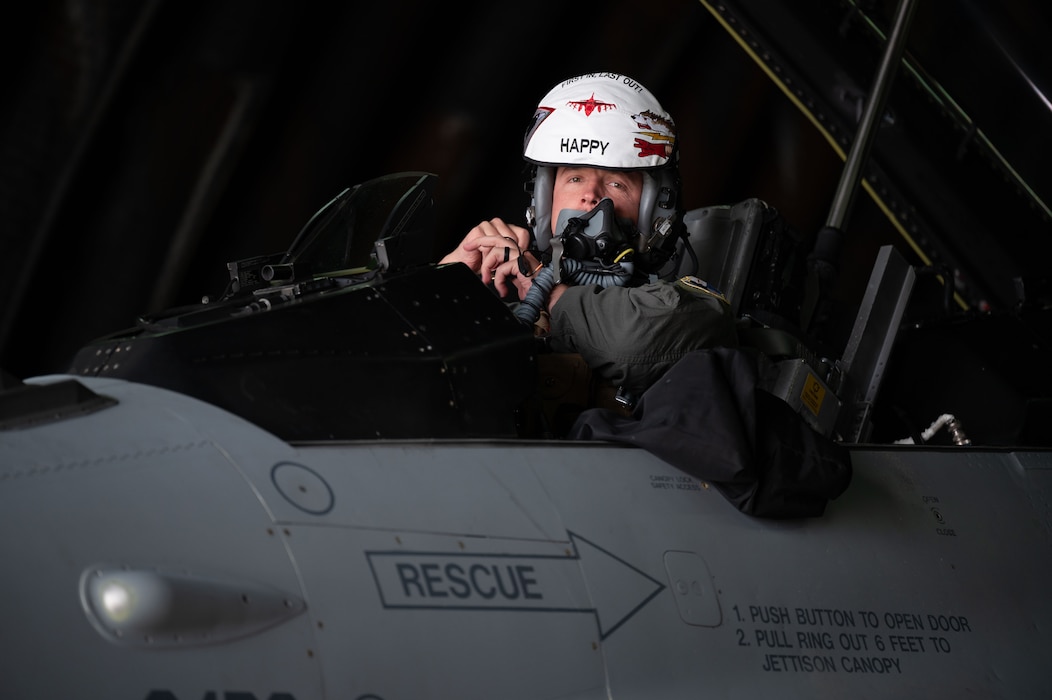 A pilot looks out from the cockpit of his aircraft while donning his helmet and mask.