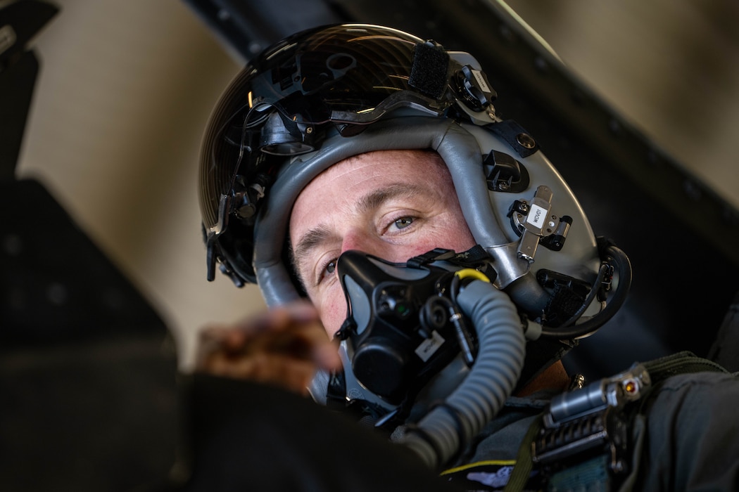 A pilot looks down from the cockpit of his fighter aircraft after donning his helmet and mask.