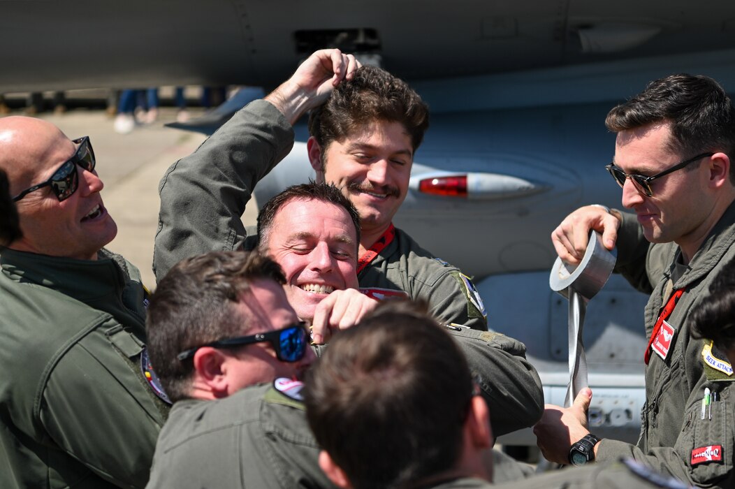 A smiling pilot is carried away from his aircraft by fellow pilots after his final flight.