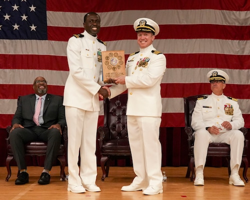 250609-O-NJ594-1011, Portsmouth, Virginia, (June 6, 2025) Lt. Ademola Ajiboye, left, an administration officer with the Navy and Marine Corps Force Health Protection Command (NMCFHPC) presents Capt. Marion Gregg, outgoing commander of NMCFHPC, former director of Defense Centers for Public Health Portsmouth (DCPH-P), center, with a plaque on behalf of the command during a change of command ceremony held on board Hampton Roads - Portsmouth Annex, June 6, 2025. Gregg will transfer to U.S. Naval Forces Central Command (COMUSNAVCENT) where he will serve as the Fifth Fleet Force Surgeon. (U.S. Navy photo by Desmond Martin)