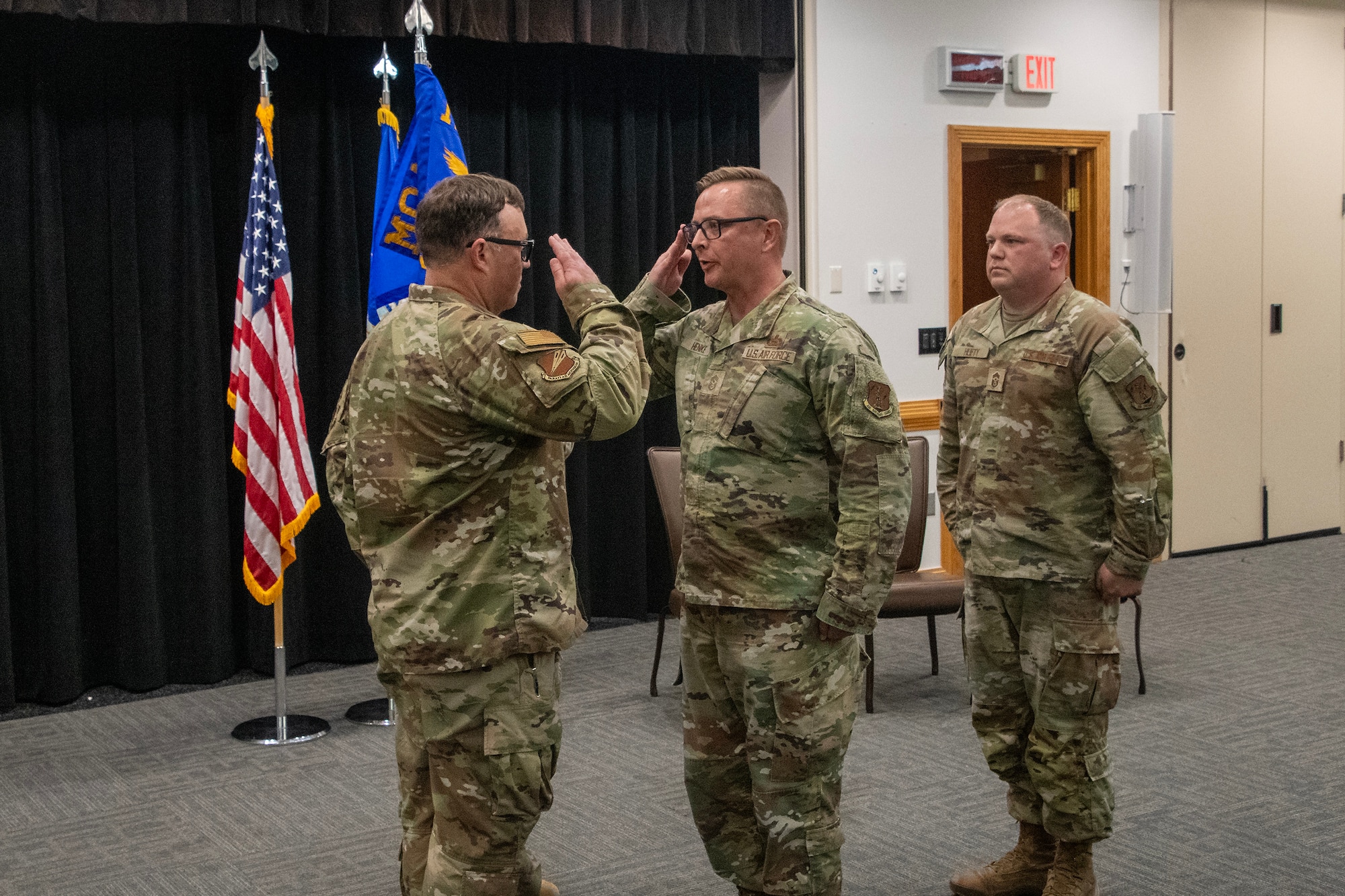 U.S. Air National Guard Airmen exchange a salute during a ceremony. They are wearing OCP pattern uniforms.