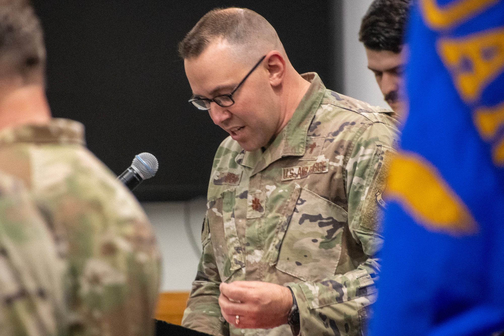 A US Air National Guard chaplain leads a group of Airmen in prayer. His head is bowed and he is wearing an OCP pattern uniform.