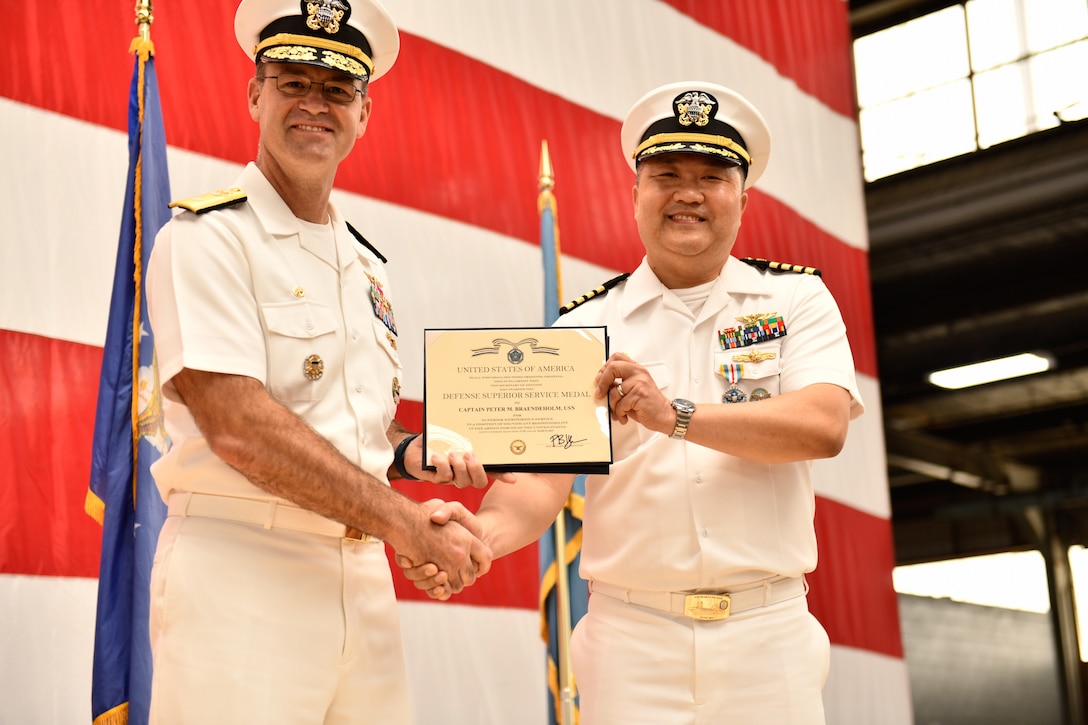 Two Navy officers shaking hands and holding an award.