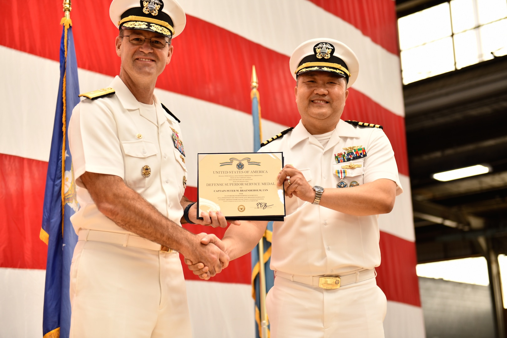 Two Navy officers shaking hands and holding an award.