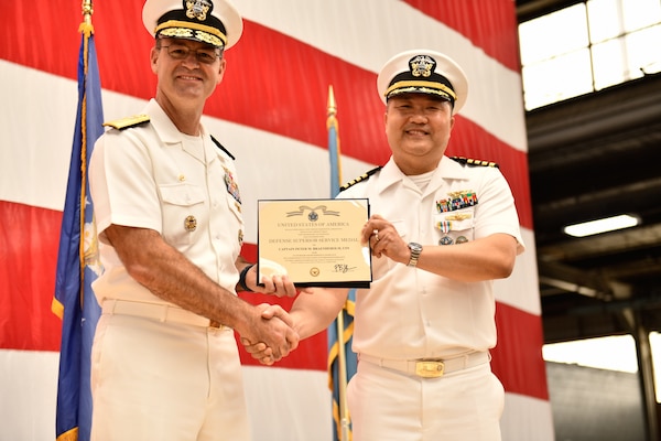 Two Navy officers shaking hands and holding an award.