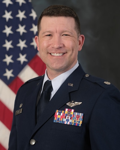 photo of uniformed U.S. Airman standing in front of a U.S. Flag