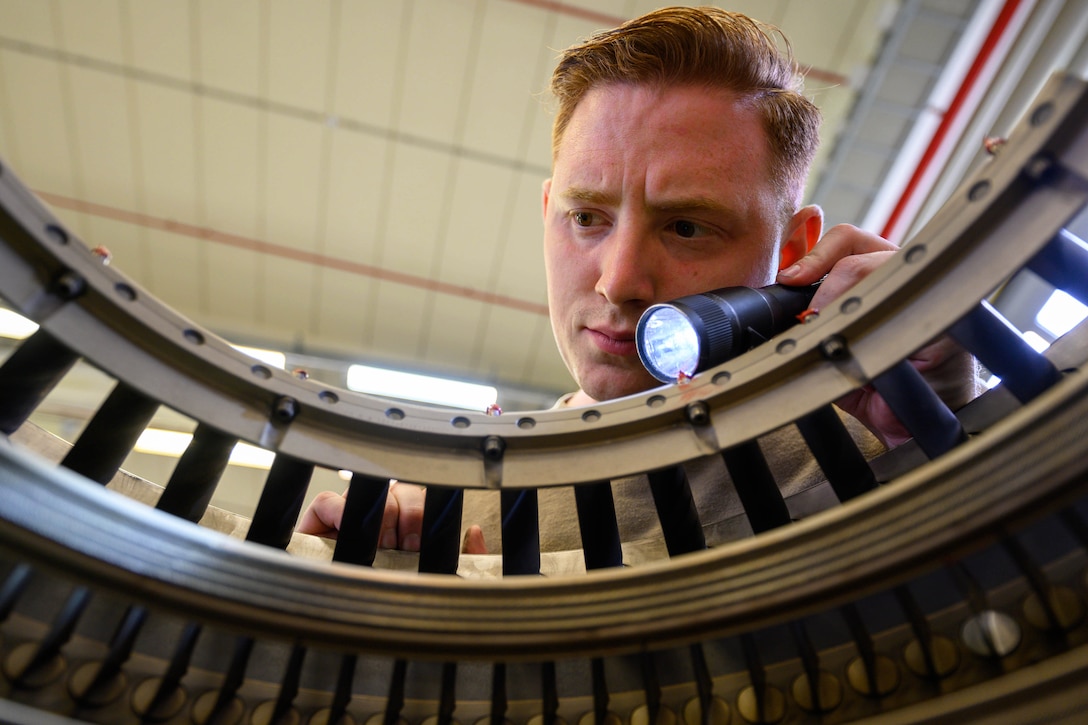 A close-up of an airman shining a flashlight on an aircraft's engine.