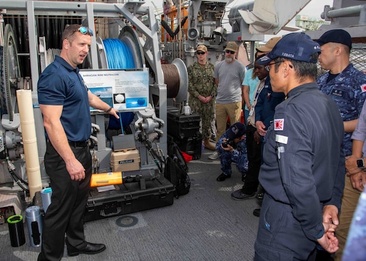 Nate Waldstein, a member of Naval Surface Warfare Center Panama City Division, describes the capabilities of the Barracuda Mine Neutralization System to Japan Maritime Self-Defense Force Rear Adm. Yatsutaka Ebata, commander, Escort Flotilla 2, and Capt. Antonio Hyde, commodore, Mine Countermeasures Squadron 7, during the Integrated Battle Problem 25.5 technology demonstration aboard the Avenger-class mine countermeasures ship USS Warrior (MCM 10), at Commander, Fleet Activities Sasebo, Japan, May 15, 2025. Exercises such as Integrated Battle Problem allow the Navy to demonstrate unmanned system operations in relevant experiment scenarios in order to meet service level objectives and operationalize unmanned systems and capabilities to maintain a secure and prosperous Indo-Pacific region. U.S. 7th Fleet, the U.S. Navy’s largest forward-deployed numbered fleet, routinely interacts and operates with allies and partners in preserving a free and open Indo-Pacific region. (U.S. Navy photo by Mass Communication Specialist 1st Class W. Chase Stephens)
