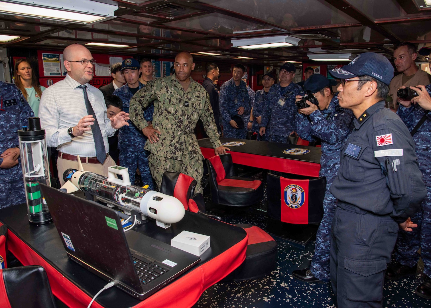 Christian Weber, the Integrated Battle Problem 25.5 technology lead from Naval Surface Warfare Center Panama City Division, describes the capabilities of the Disposable Reusable Expeditionary Warfare Underwater Vehicle (DREW-UV) to Japan Maritime Self-Defense Force Rear Adm. Yatsutaka Ebata, commander, Escort Flotilla 2, and Capt. Antonio Hyde, commodore, Mine Countermeasures Squadron 7, during the Integrated Battle Problem 25.5 technology demonstration aboard the Avenger-class mine countermeasures ship USS Warrior (MCM 10), at Fleet Activities Sasebo, Japan, May 15, 2025. Exercises such as Integrated Battle Problem allow the Navy to demonstrate unmanned system operations in relevant experiment scenarios to meet service level objectives and operationalize unmanned systems and capabilities to maintain a secure and prosperous Indo-Pacific region. U.S. 7th Fleet, the U.S. Navy’s largest forward-deployed numbered fleet routinely interacts and operates with allies and partners in preserving a free and open Indo-Pacific region. (U.S. Navy photo by Mass Communication Specialist 1st Class W. Chase Stephens. Portions of this photo have been obscured for security purposes.)