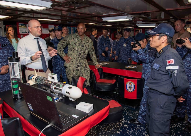 Christian Weber, the Integrated Battle Problem 25.5 technology lead from Naval Surface Warfare Center Panama City Division, describes the capabilities of the Disposable Reusable Expeditionary Warfare Underwater Vehicle (DREW-UV) to Japan Maritime Self-Defense Force Rear Adm. Yatsutaka Ebata, commander, Escort Flotilla 2, and Capt. Antonio Hyde, commodore, Mine Countermeasures Squadron 7, during the Integrated Battle Problem 25.5 technology demonstration aboard the Avenger-class mine countermeasures ship USS Warrior (MCM 10), at Fleet Activities Sasebo, Japan, May 15, 2025. Exercises such as Integrated Battle Problem allow the Navy to demonstrate unmanned system operations in relevant experiment scenarios to meet service level objectives and operationalize unmanned systems and capabilities to maintain a secure and prosperous Indo-Pacific region. U.S. 7th Fleet, the U.S. Navy’s largest forward-deployed numbered fleet routinely interacts and operates with allies and partners in preserving a free and open Indo-Pacific region. (U.S. Navy photo by Mass Communication Specialist 1st Class W. Chase Stephens. Portions of this photo have been obscured for security purposes.)
