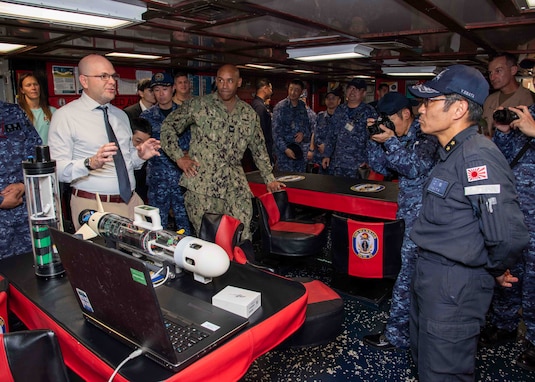 Christian Weber, the Integrated Battle Problem 25.5 technology lead from Naval Surface Warfare Center Panama City Division, describes the capabilities of the Disposable Reusable Expeditionary Warfare Underwater Vehicle (DREW-UV) to Japan Maritime Self-Defense Force Rear Adm. Yatsutaka Ebata, commander, Escort Flotilla 2, and Capt. Antonio Hyde, commodore, Mine Countermeasures Squadron 7, during the Integrated Battle Problem 25.5 technology demonstration aboard the Avenger-class mine countermeasures ship USS Warrior (MCM 10), at Fleet Activities Sasebo, Japan, May 15, 2025. Exercises such as Integrated Battle Problem allow the Navy to demonstrate unmanned system operations in relevant experiment scenarios to meet service level objectives and operationalize unmanned systems and capabilities to maintain a secure and prosperous Indo-Pacific region. U.S. 7th Fleet, the U.S. Navy’s largest forward-deployed numbered fleet routinely interacts and operates with allies and partners in preserving a free and open Indo-Pacific region. (U.S. Navy photo by Mass Communication Specialist 1st Class W. Chase Stephens. Portions of this photo have been obscured for security purposes.)