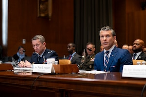 Two men sit in front of microphones at a table during a hearing.