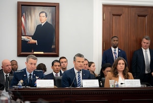 Three people sit at a table with microphones during a hearing. 
