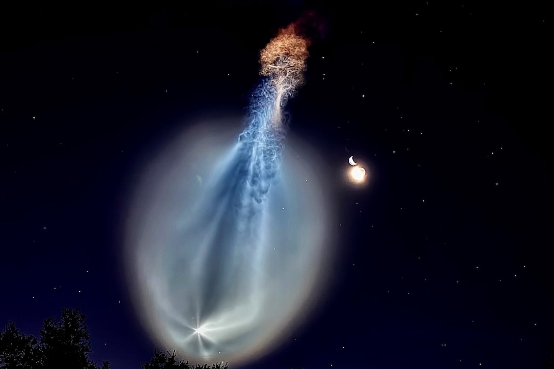 A rocket launches into a dark sky, creating an illuminating trail with stars in the background.