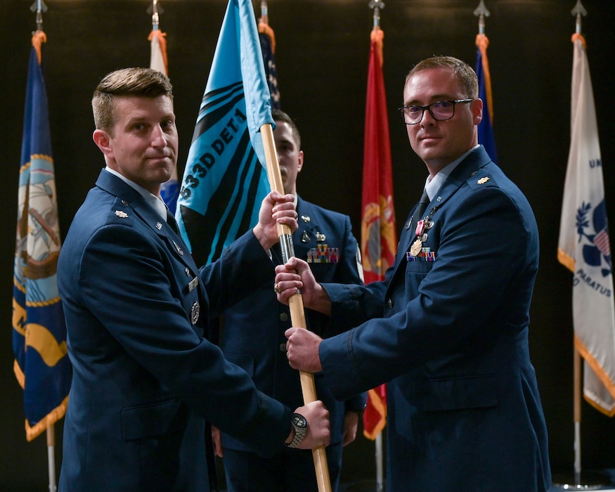 U.S. Space Force Lt. Col. Adam P. Jodice, left, 533rd Training Squadron commander, takes the 533rd TRS, Detachment 1 guidon from Maj. Benjamin Tillman, right, departing commander, during the 533rd, Detachment 1 Change of Command Ceremony at the Powell Event Center, Goodfellow Air Force Base, Texas, June 10, 2025. Tillman assumed command on Aug. 29, 2023. (U.S. Air Force photo by Senior Airman Evelyn J. D’Errico)