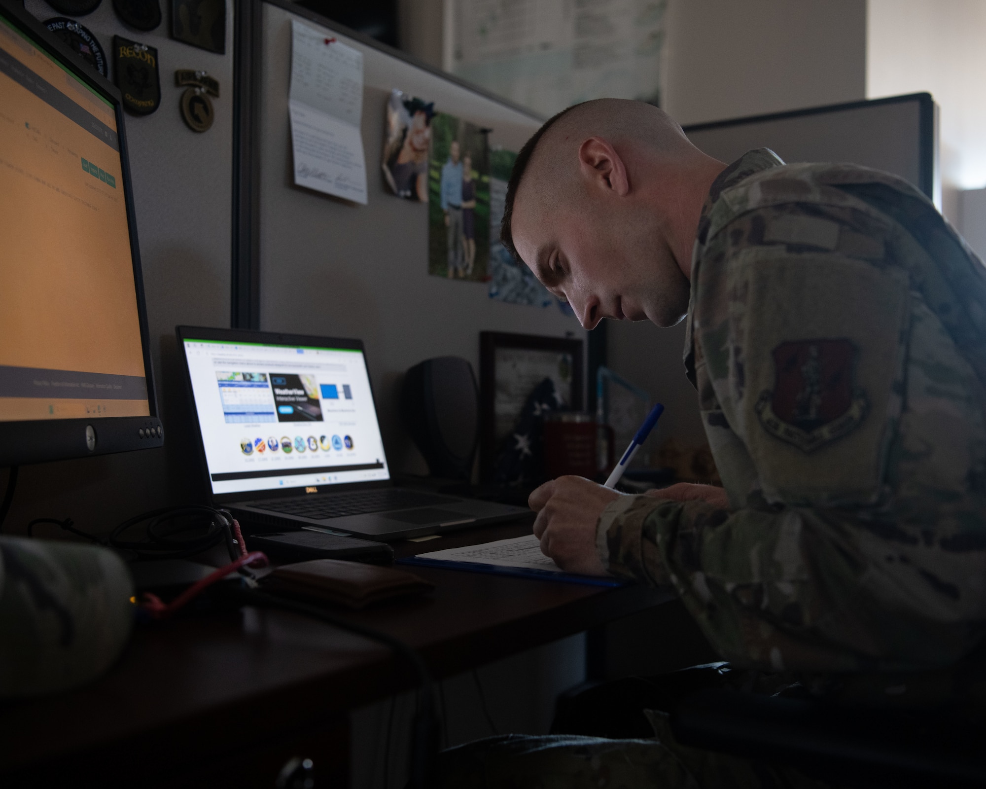 Airman writing on paper with computer open in front of him