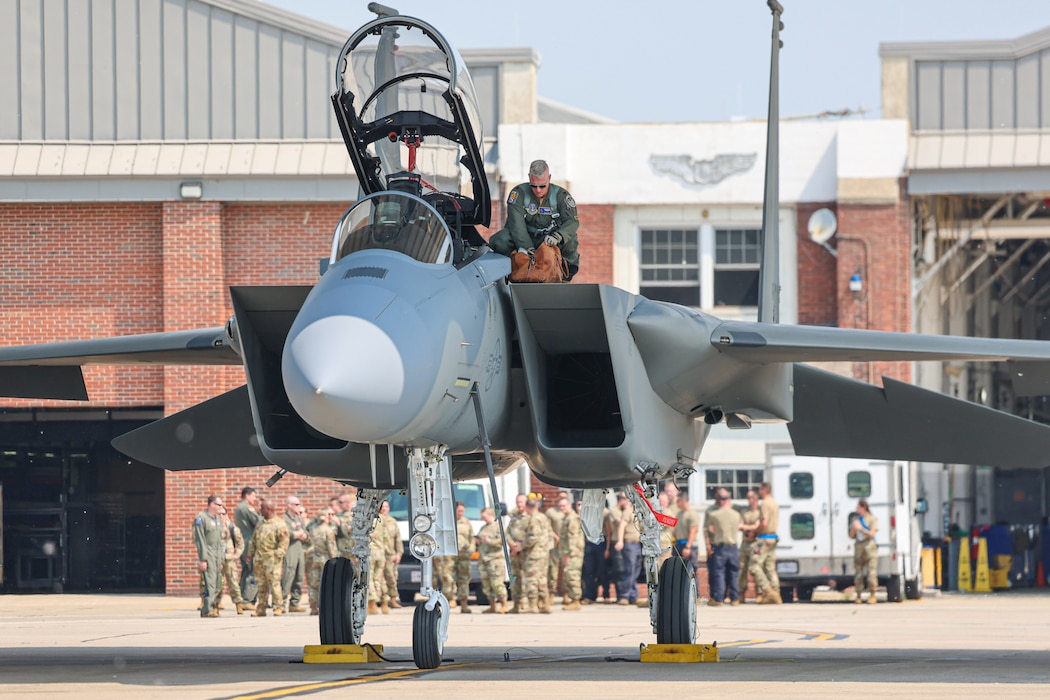 Pilot crouches on wing of F-15EX aircraft.