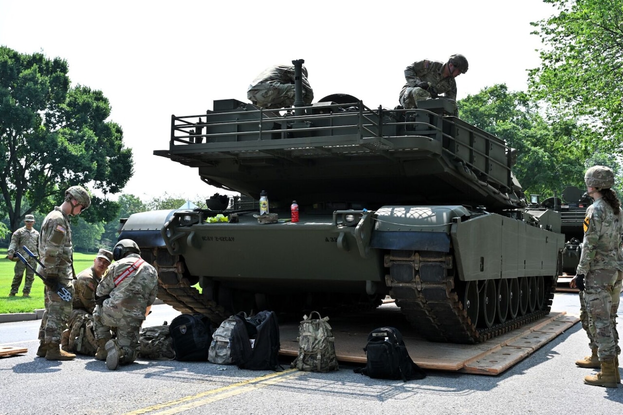 A group of men and women in camouflage military uniforms are working outdoors on a large military vehicle.
