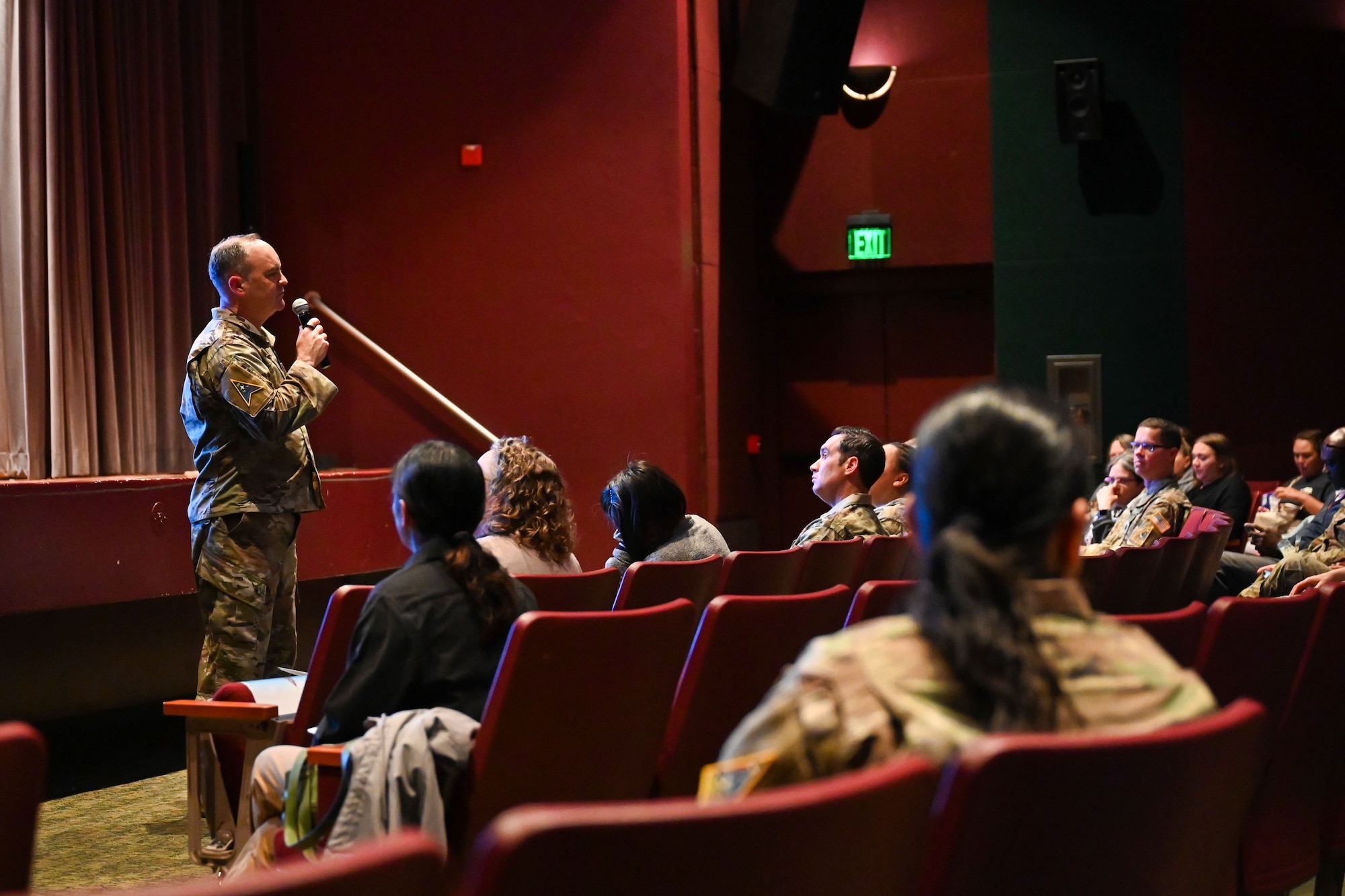 People listen to a standing speaker inside a theater.