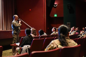 People listen to a standing speaker inside a theater.