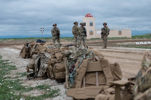  Security forces members stand talking next to a line of military bags.
