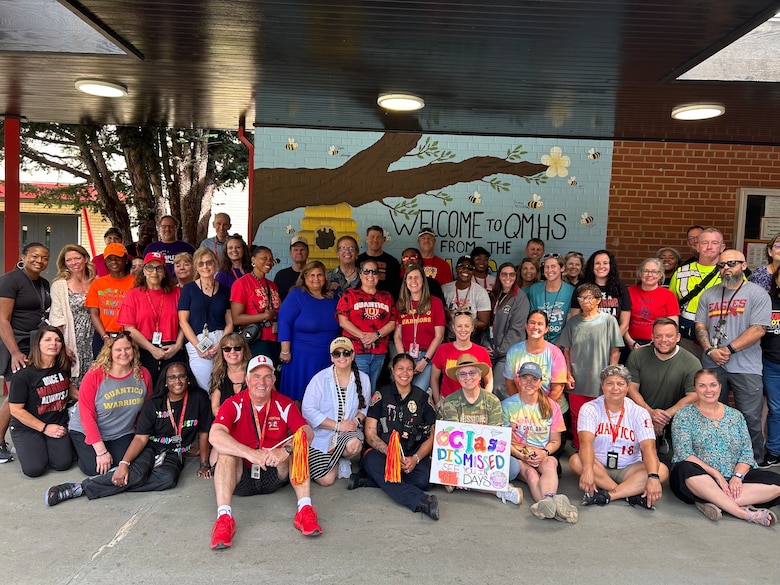Miles Shae (seated wearing red shirt and a white hat), the Quantico Middle High School principal, and QMHS staff take one last photo as the 2024-2025 school year comes to an end, June 10, 2025. Shae was awarded the DoD Education Activity Americas’ 2025 Principal of the Year for his service and dedication to military-connected students. The DoDEA Principal of the Year Program honors exceptional school principals from three regions: the Americas, Europe, and Pacific regions; each selectee must have demonstrated leadership in creating high-quality learning experiences for students and made significant contributions to the education profession. "I have simply had the opportunity to be a member of that team, and I have been fortunate to accept such a prestigious award on behalf of the entire Marine Corps Base Quantico community.” (Courtesy photo by QMHS staff)