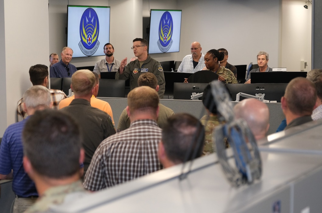 photo of a large room with people standing listening to a US Airman speak