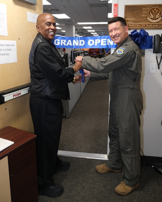 photo of uniformed US Airman and civilian cutting a grand opening ribbon with large scissors