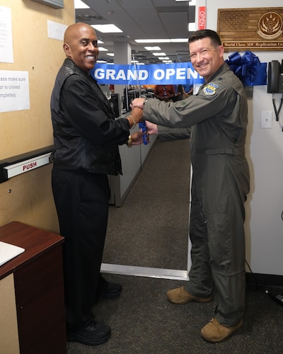 photo of uniformed US Airman and civilian cutting a grand opening ribbon with large scissors